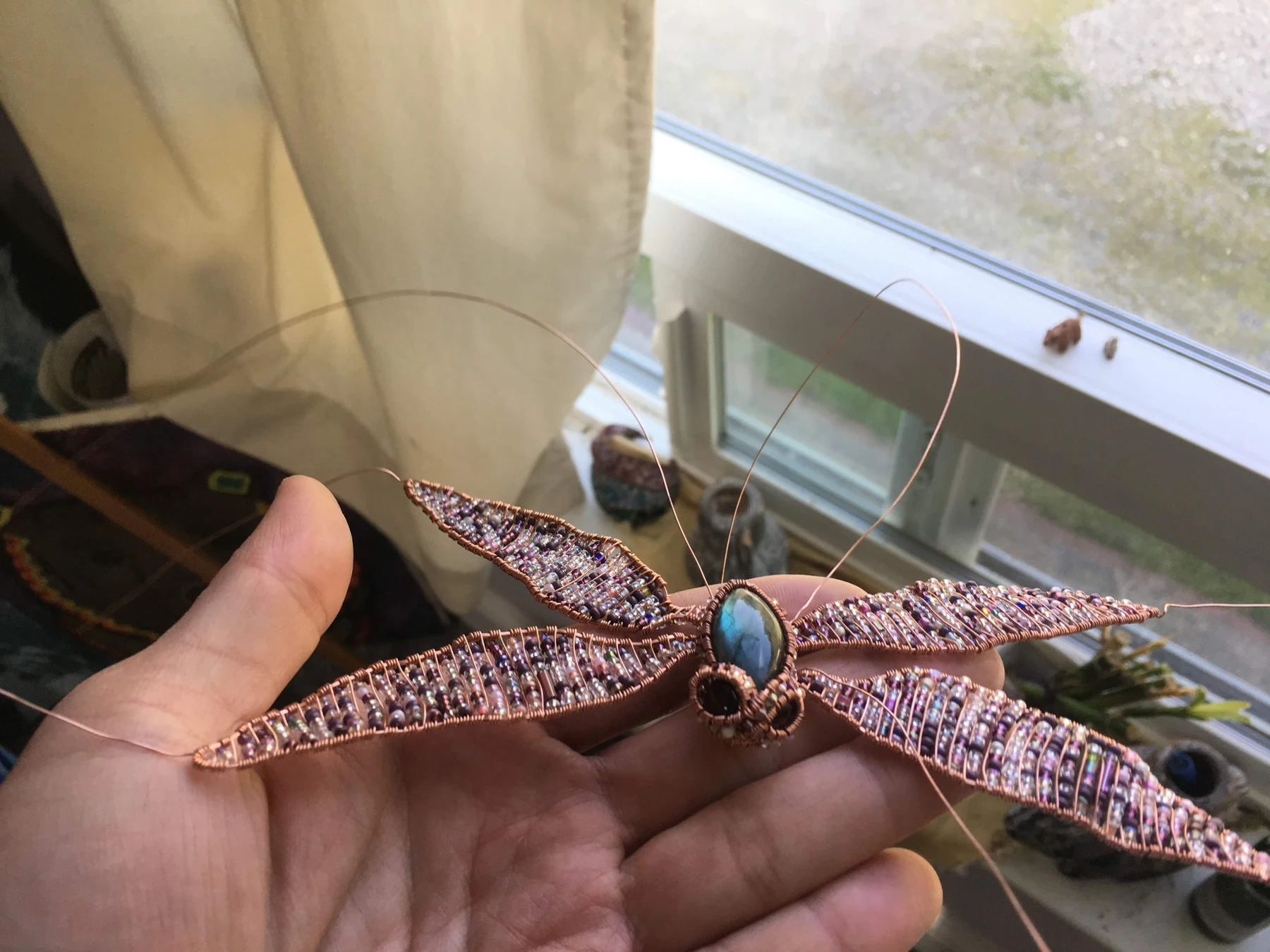 The handmade dragonfly resting across an open hand, showing its scale.